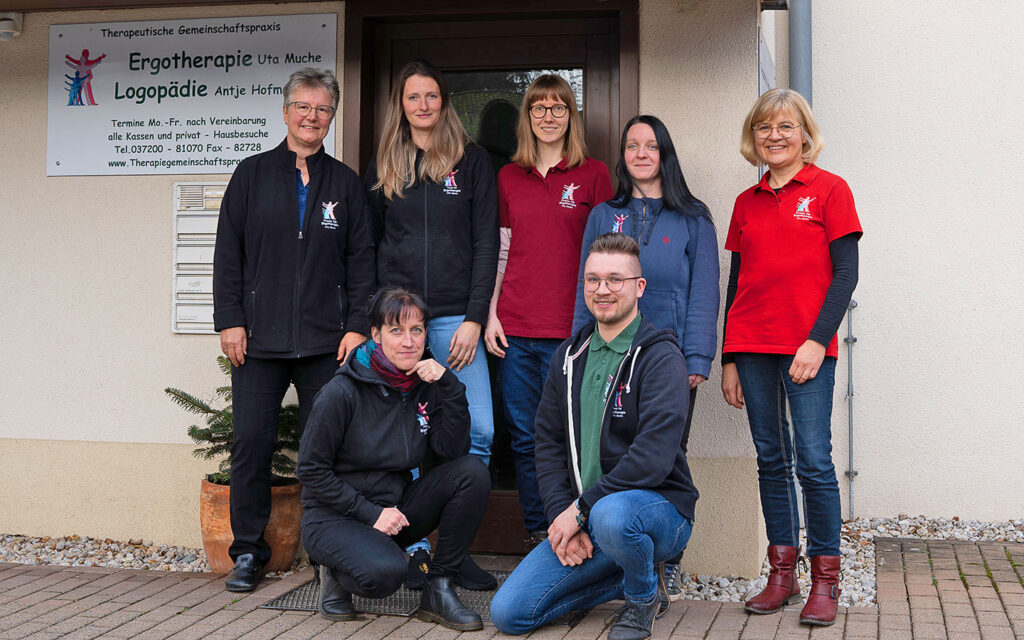 Ein Gruppenfoto vom Team. Das gesamte Team steht vor dem Eingang der Praxis